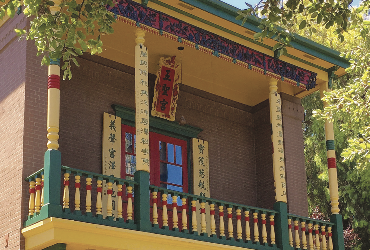 A picture of a Chinese-style temple balcony, painted in vibrant red, green, and yellow tones and surrounded by green foliage