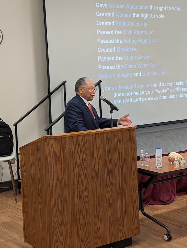 man speaking at podium in front of screen