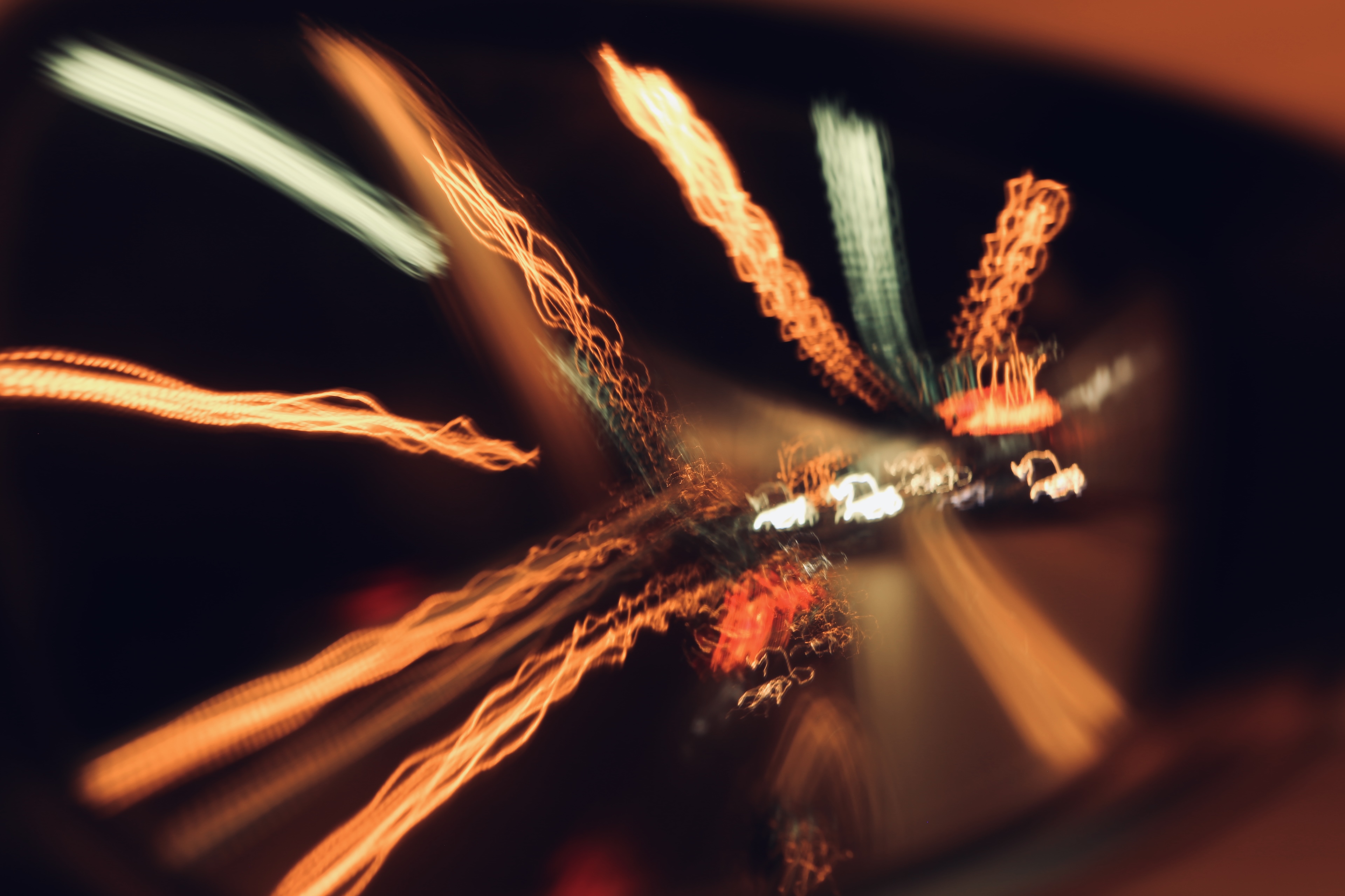 Long-exposure night photography showing streaking car lights radiating outward from a central vanishing point on a dark road from glasses reflection
