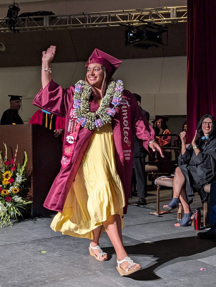 young woman waving as she walks across stage